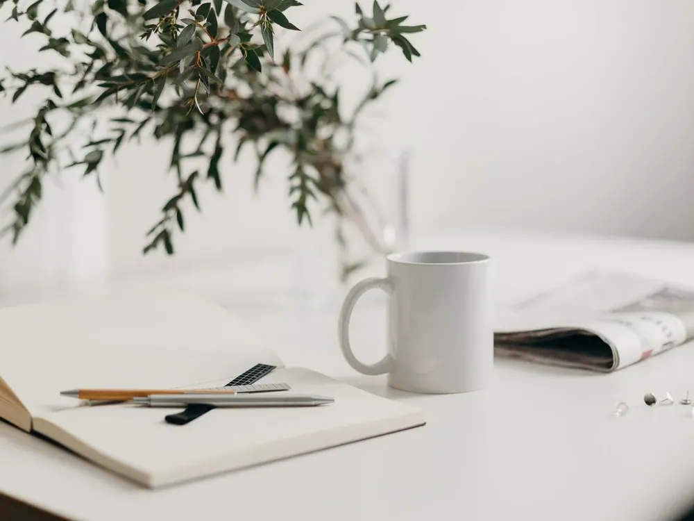 Bureau blanc lumineux avec un carnet, un stylo, une tasse et une plante