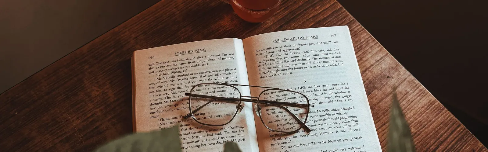 Livre ouvert, lunettes et tasse de thé sur une table en bois